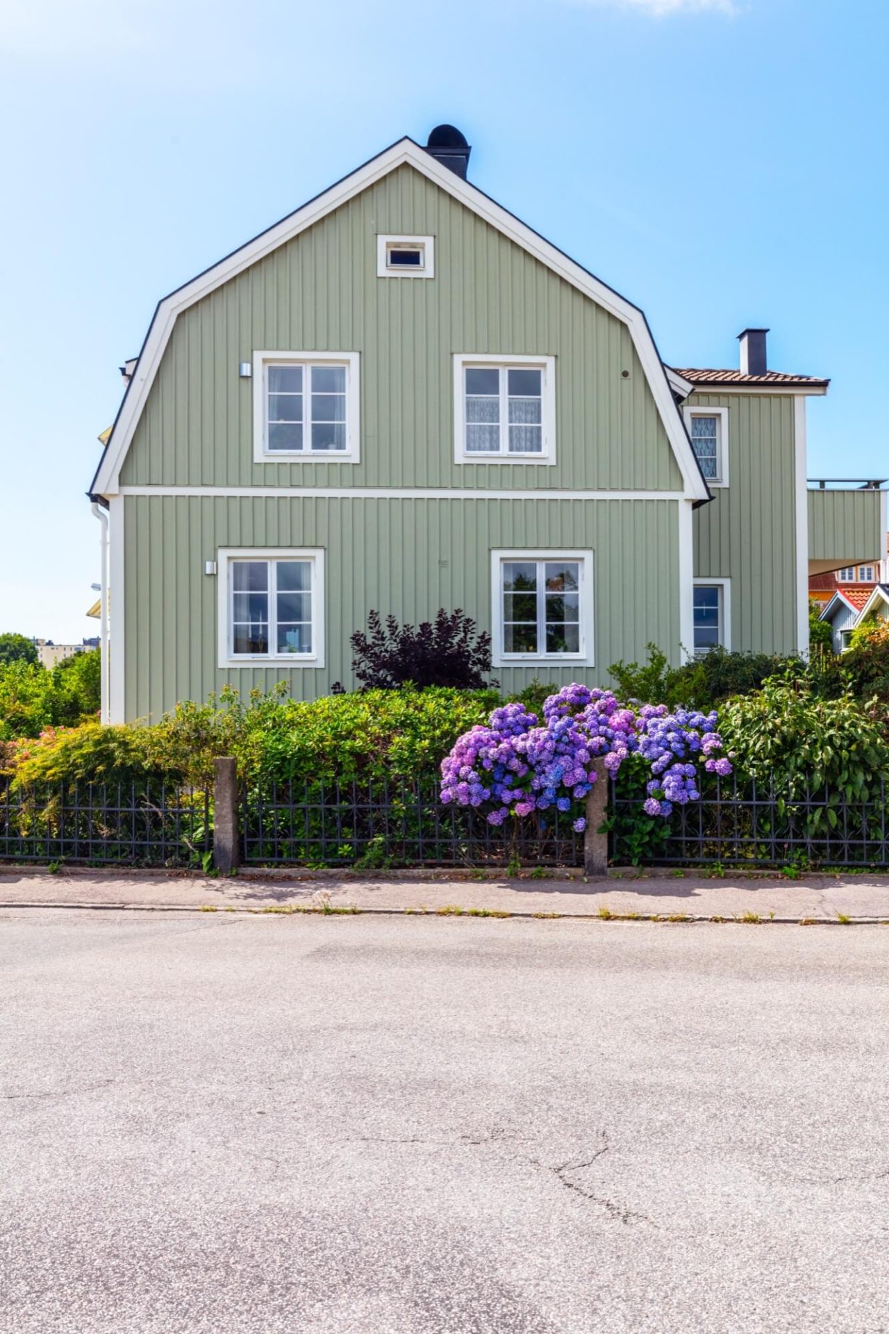 En byggnad med träpaneler målade grönt, vita dekorationer längs fasaden, och en trädgård överflödande med blommande lila hortensior